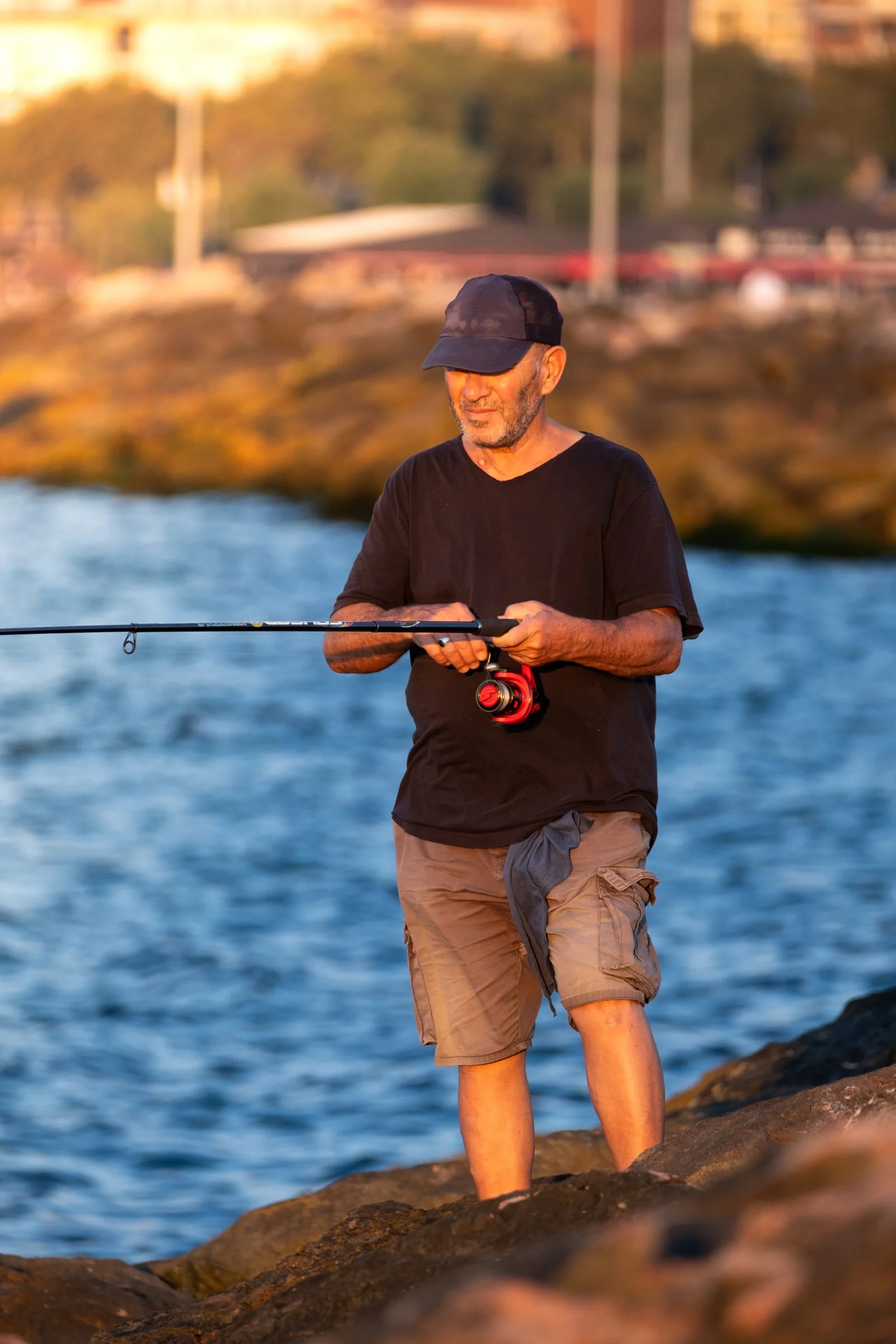 An older angler beside a rocky shoreline in warm light