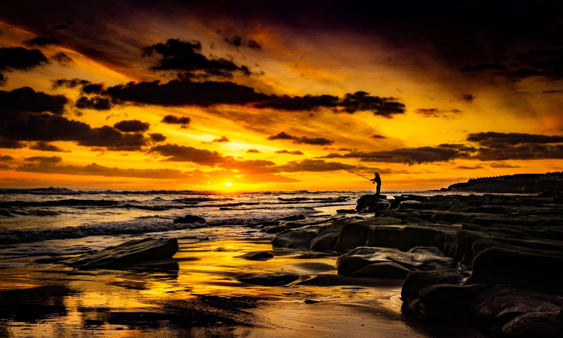 A silhouetted angler casting beside a sunset coastline