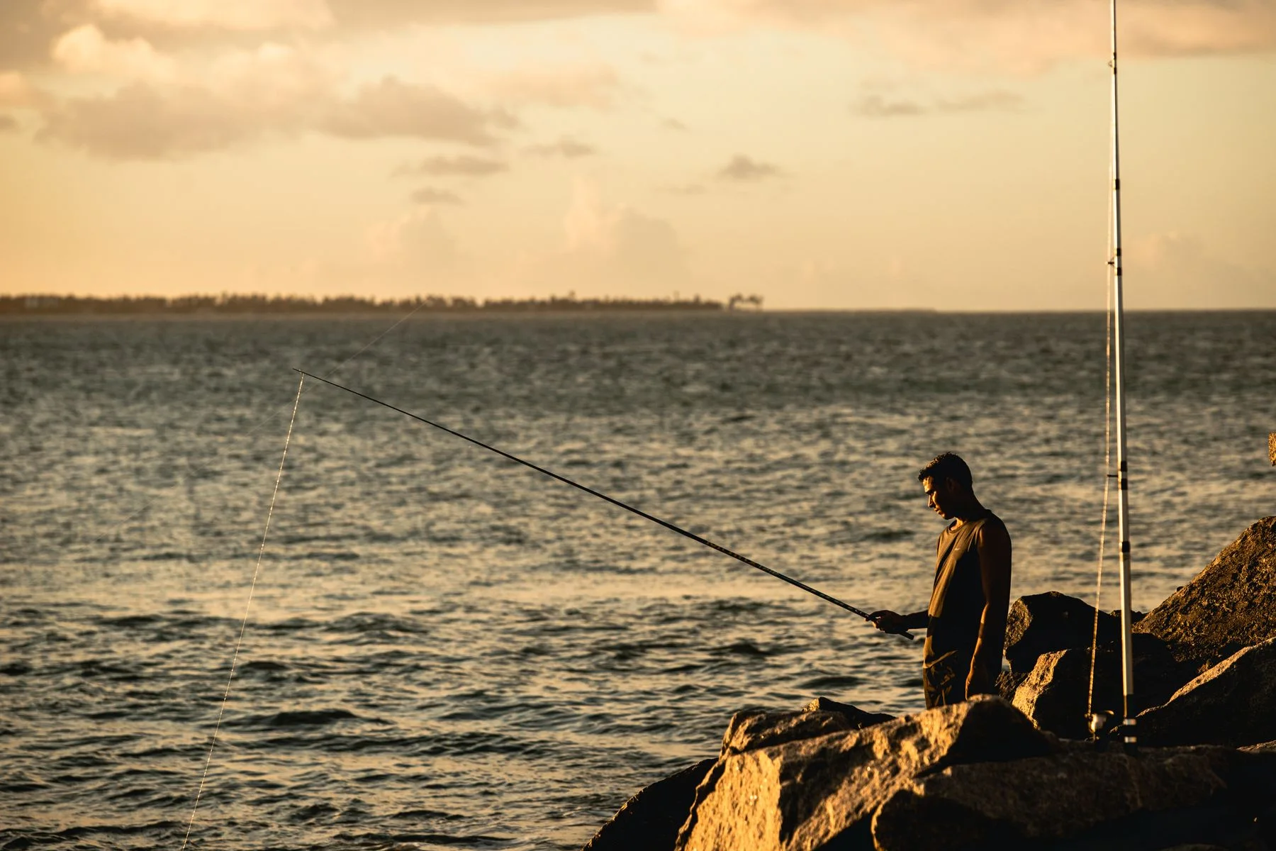 A lone angler fishing from a rocky shore at dusk