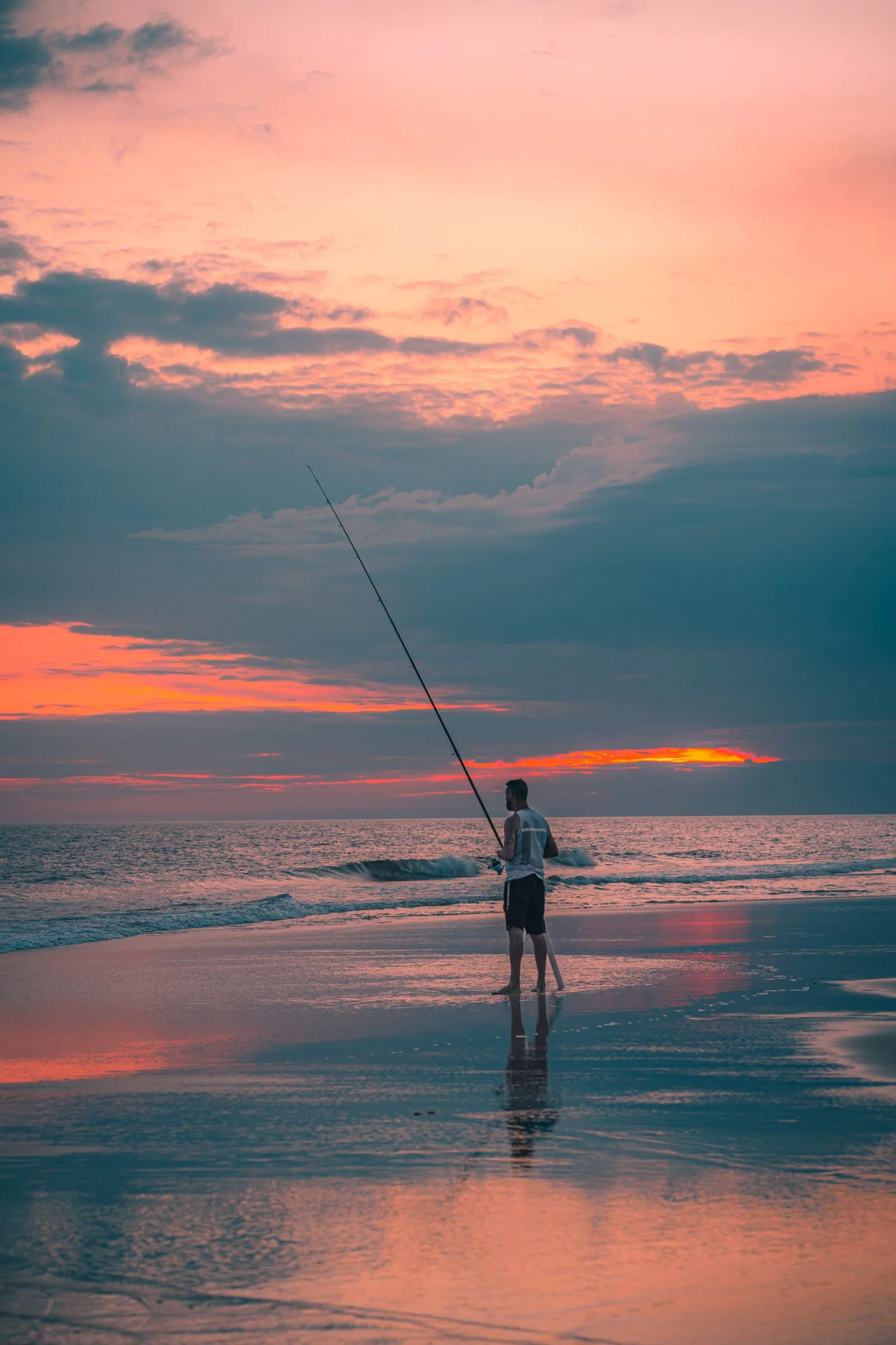 An angler on a quiet beach beneath pastel evening skies