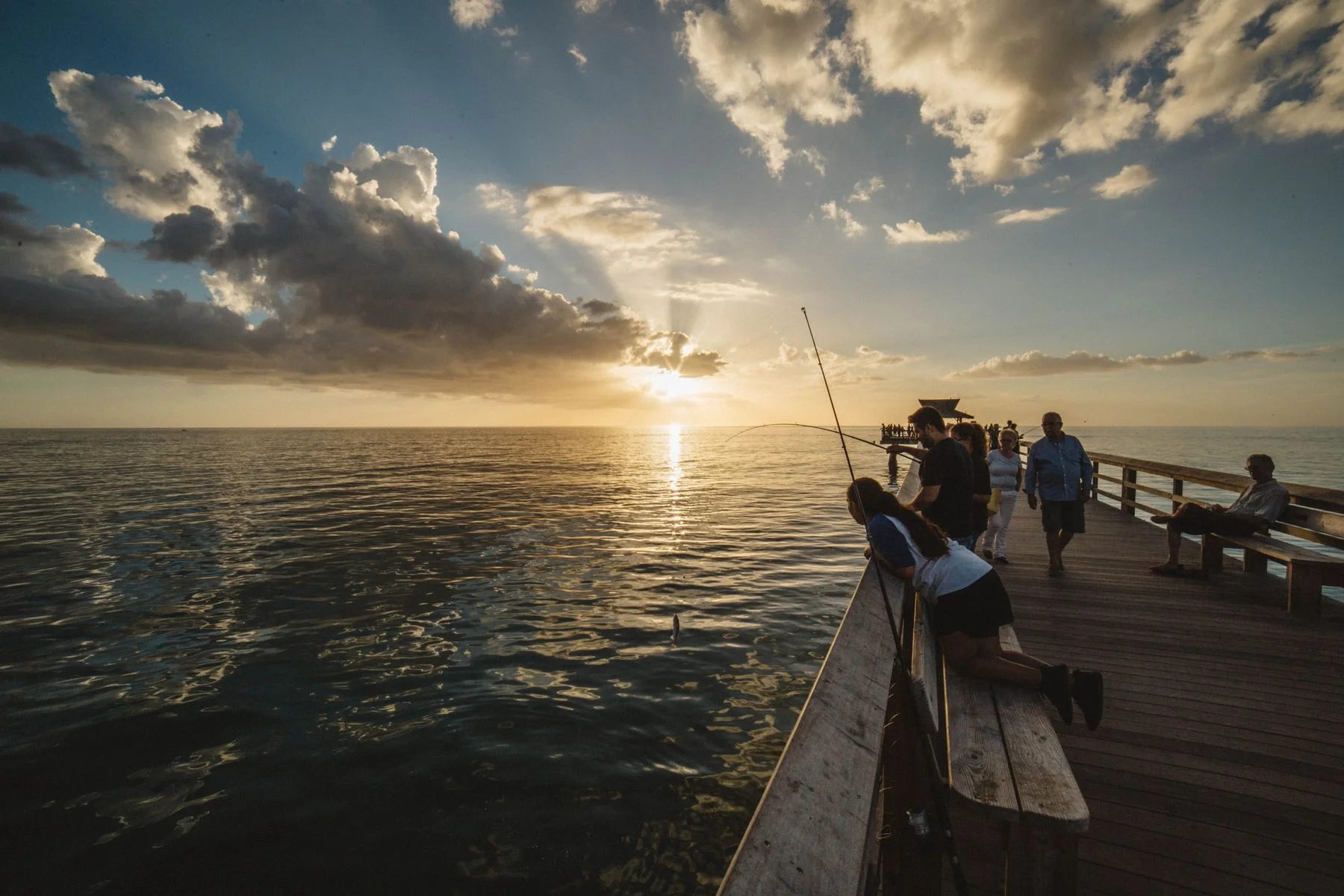 People fishing from a wooden pier at sunset