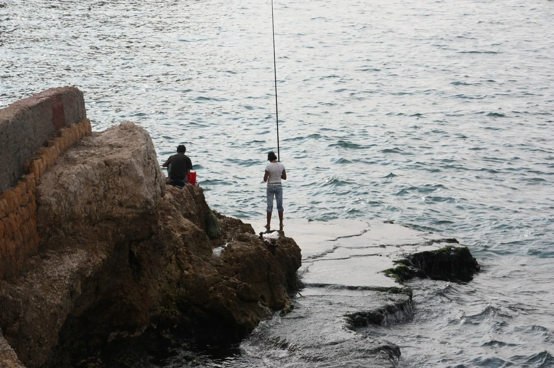 Two anglers fishing from rocks beside the ocean